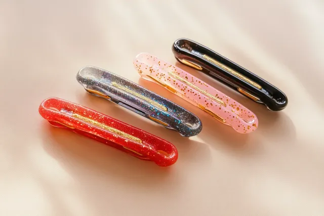 Four glitter hair clips in red, gray, pink, and black lying on soft beige fabric.