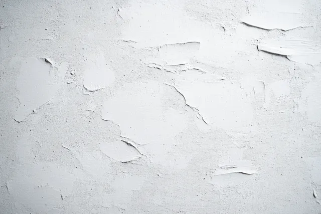 White plaster wall close-up with rough uneven texture and cracks forming abstract patterns.