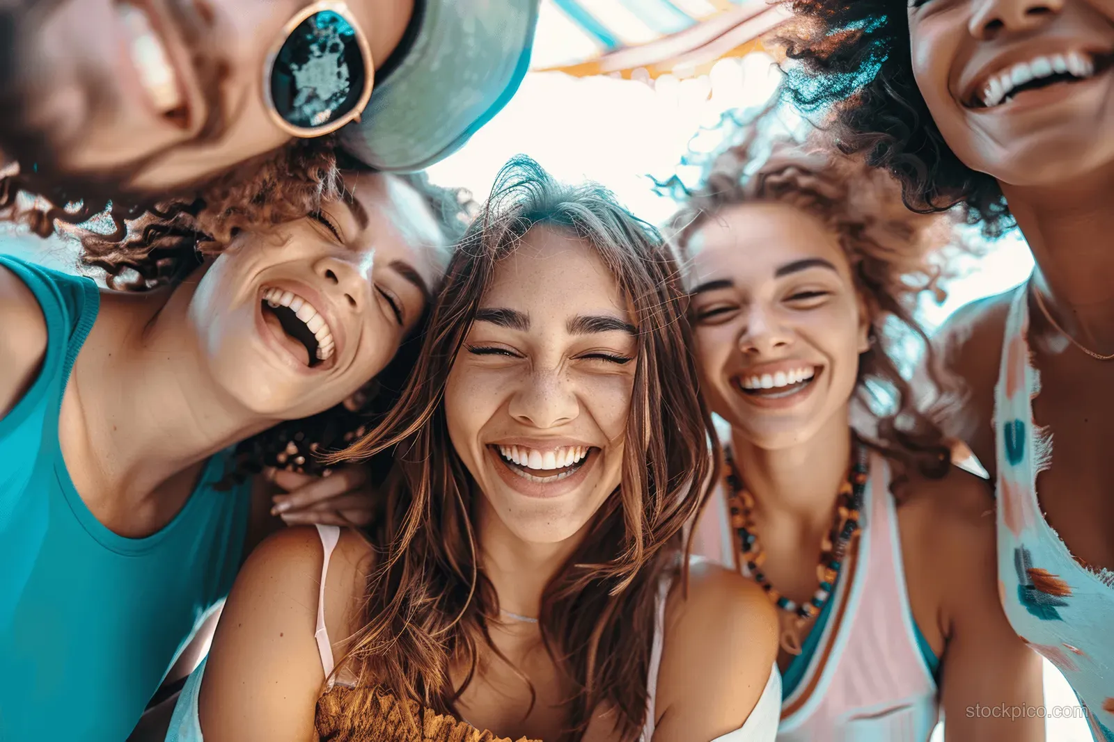 Multiracial group of friends laughs together while taking an outdoor selfie in sunny daylight.