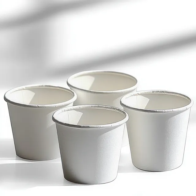 Four empty white paper cups closely grouped on a bright white surface with soft shadows.