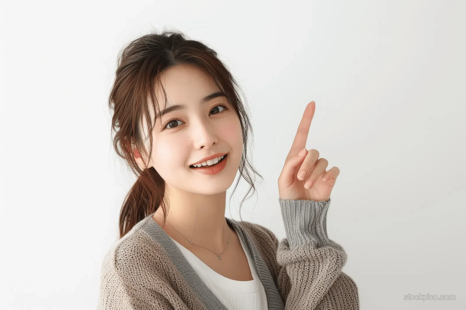 Smiling Japanese businesswoman pointing upward in a studio portrait against a plain white background.