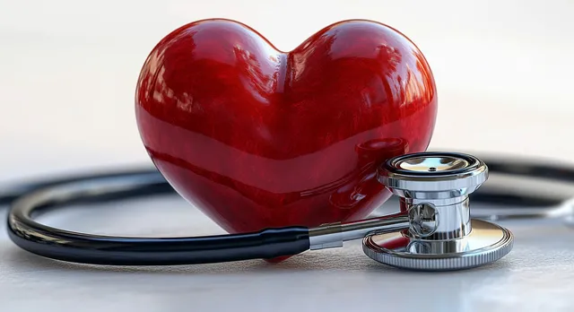 Shiny red heart sculpture beside metallic stethoscope on a pale clinical surface