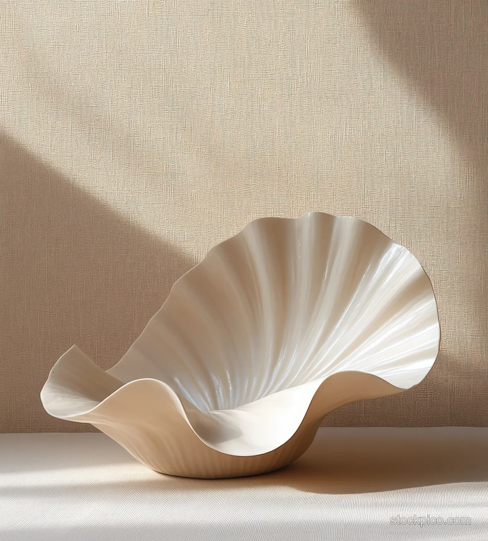 A minimalist seashell sculpture sits on a beige pedestal with soft shadows against a warm background.