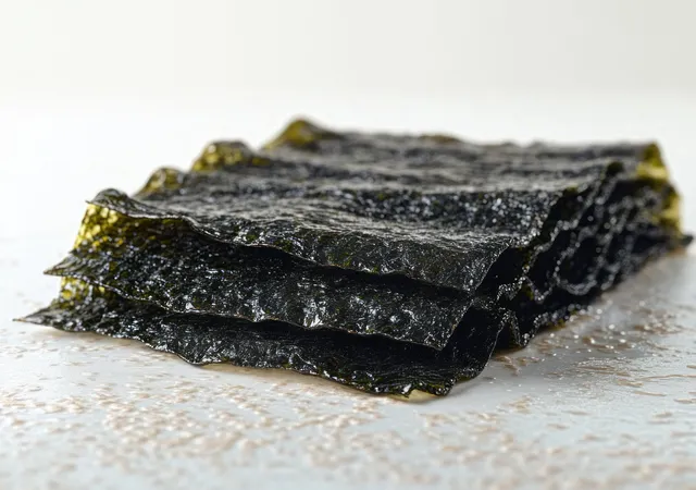 Crispy dark green dried seaweed sheets stacked on a light surface with small salt grains scattered around.
