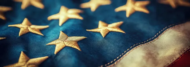 Close-up American flag fabric with gold stars and a warm vintage sunlight glow.