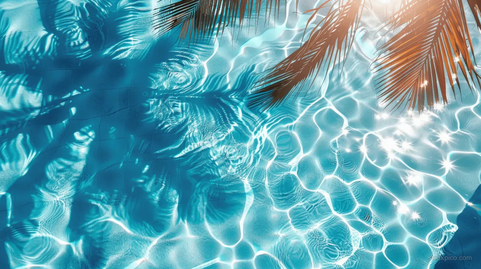 Turquoise pool water surface with bright sun glare and palm leaf shadows forming ripple patterns.