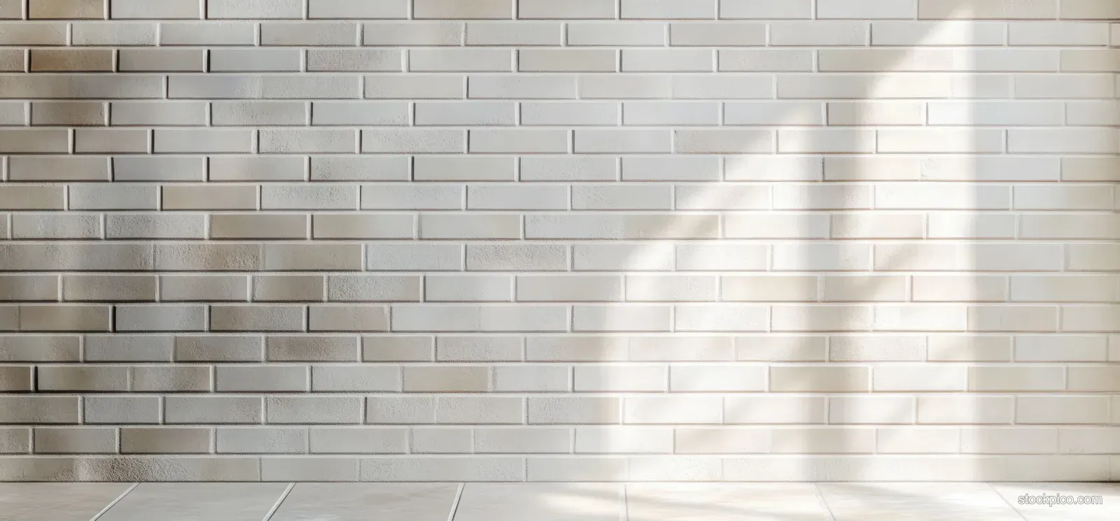 Sunlight creates soft shadow stripes on a white brick wall and tiled floor.