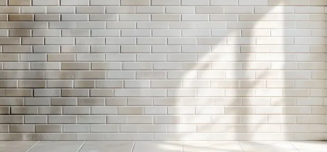 Sunlight creates soft shadow stripes on a white brick wall and tiled floor.