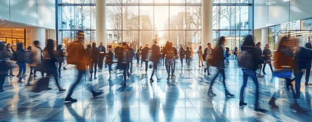 Students walk through a university lobby, motion blur and sunlight near large windows