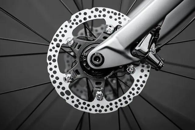 Disc brake rotor and wheel hub with thin spokes in sharp focus on a dark blurred background.