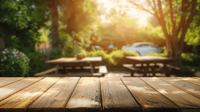 Wooden picnic table in sunny greenery with blurred outdoor tables in the background.