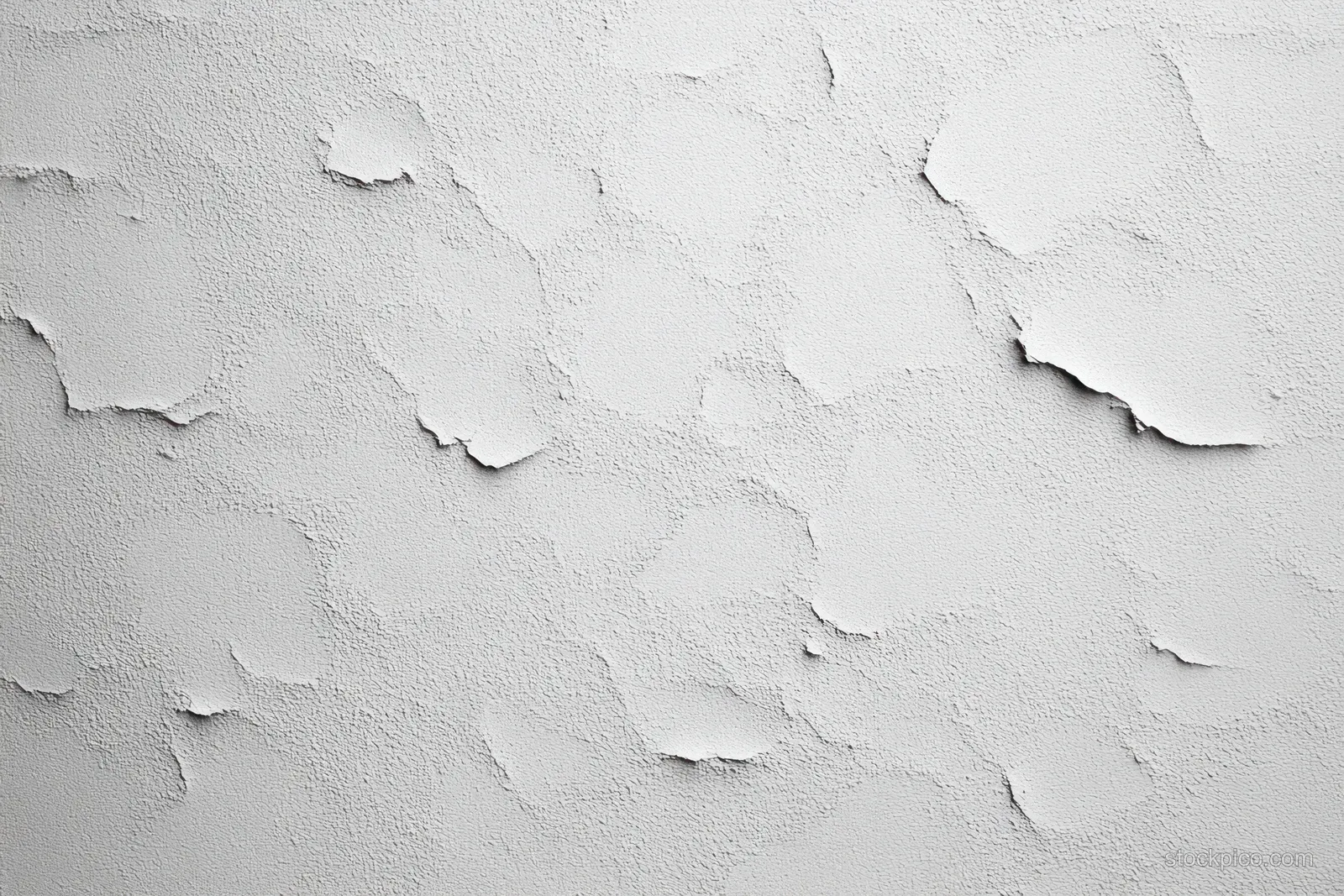 White paint peels away on a rough wall, revealing flaking layers and chipped patches.