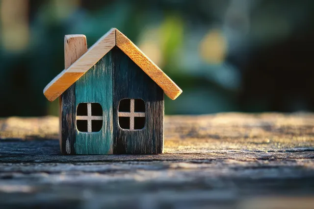 Mini wooden house with teal walls and black window openings placed on a weathered rustic plank.
