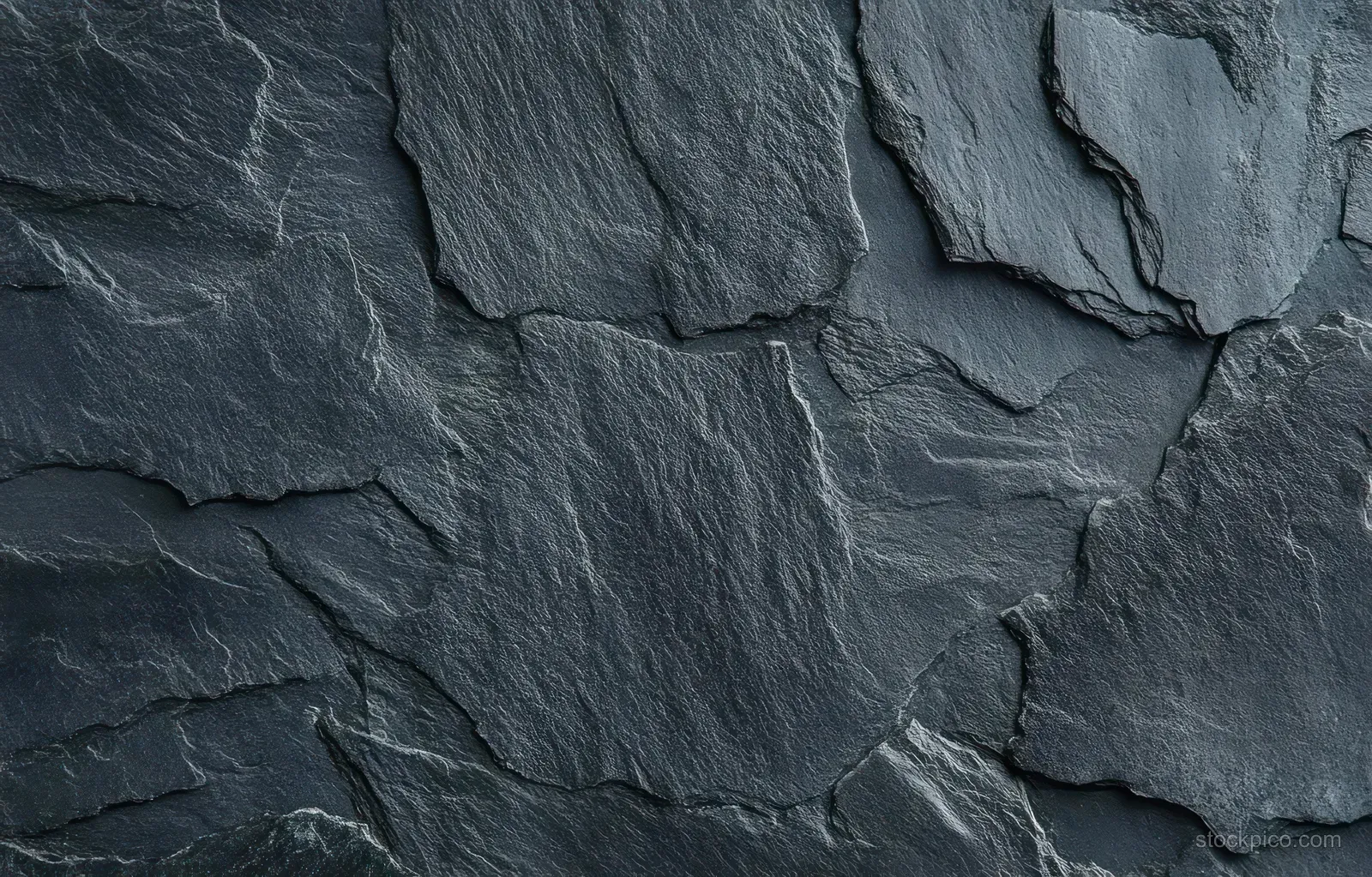 Overlapping dark gray slate stones in a rough wall surface with visible cracks and layered seams.