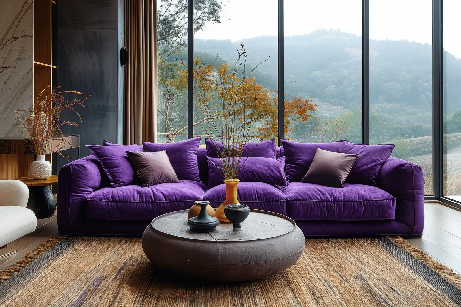 Purple velvet sofa, beige armchair, and round coffee table in a bright living room with tall grid windows and hillside view.
