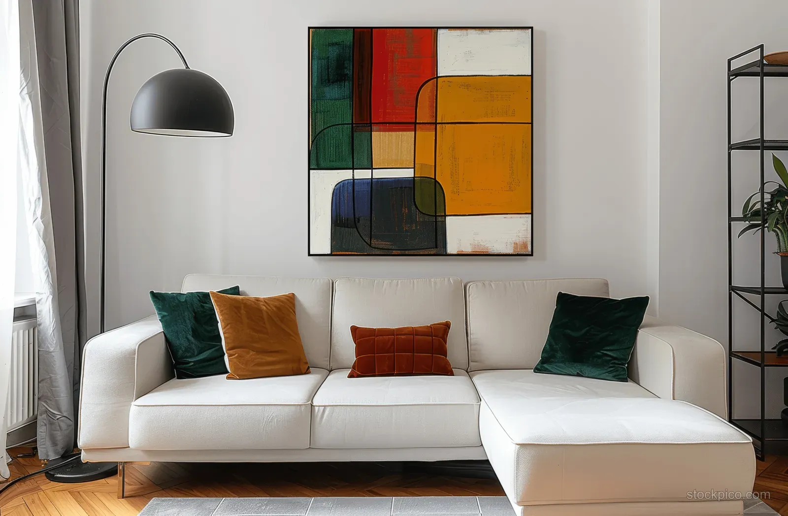White sofa with green velvet cushions sits under an abstract wall painting, with a black floor lamp and wooden shelves nearby.