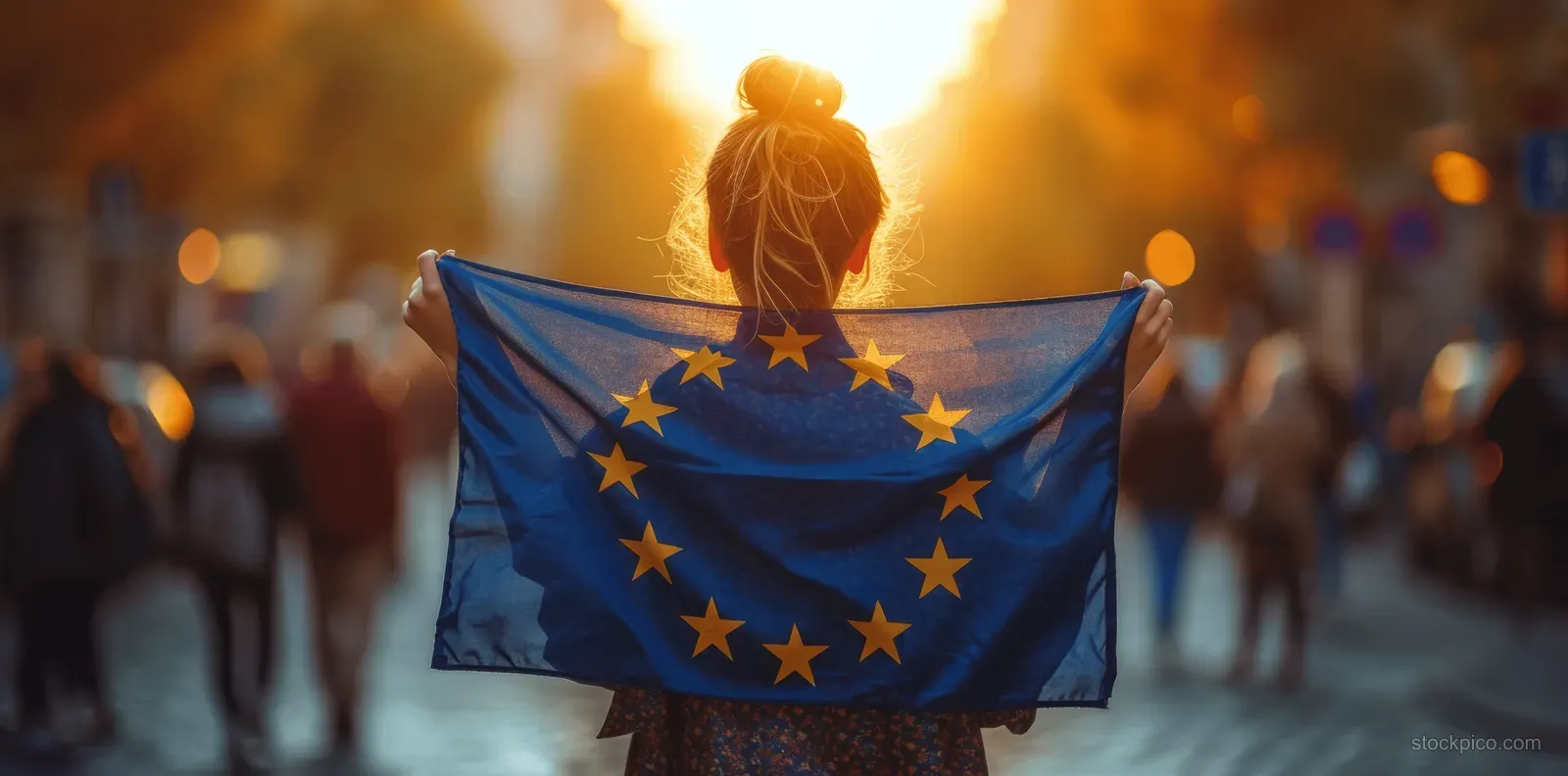 A young woman holds a European Union flag during a city street protest at golden hour.