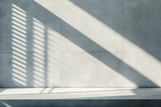 Empty minimalist interior with textured concrete wall and diagonal window blind shadows across a smooth floor.