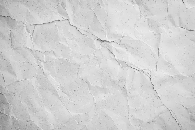White concrete wall close-up with fine gray cracks and mottled plaster texture.