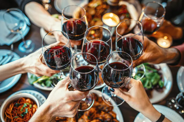 Friends clink red wine glasses over a dinner table filled with food during a Ramadan celebration.