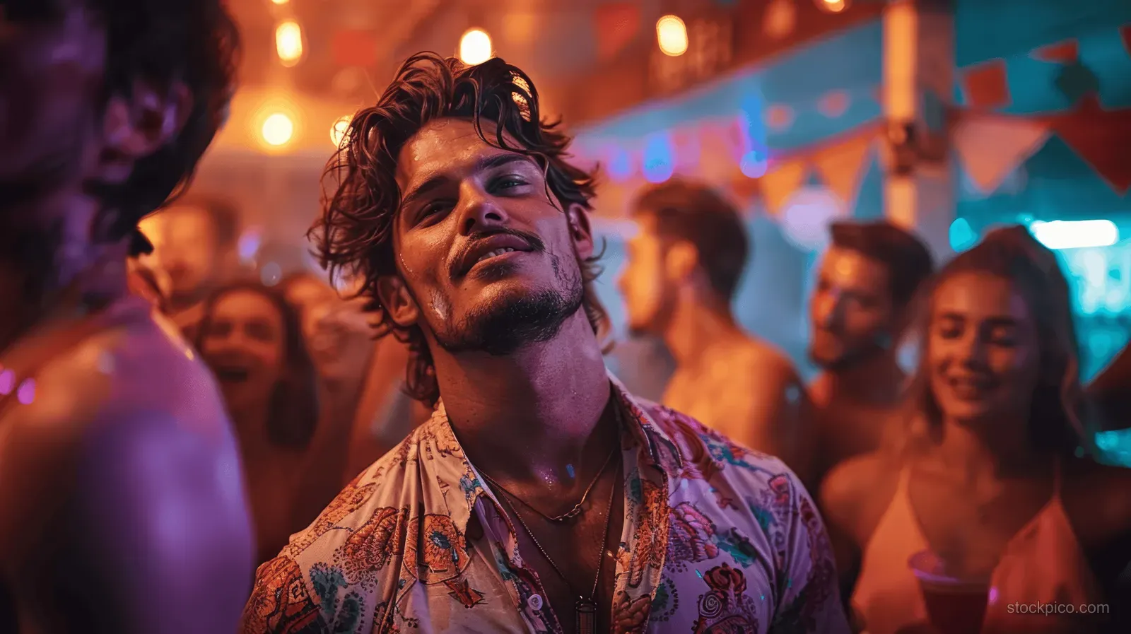 Young man dances in a neon-lit nightclub with blurred partygoers in the background.