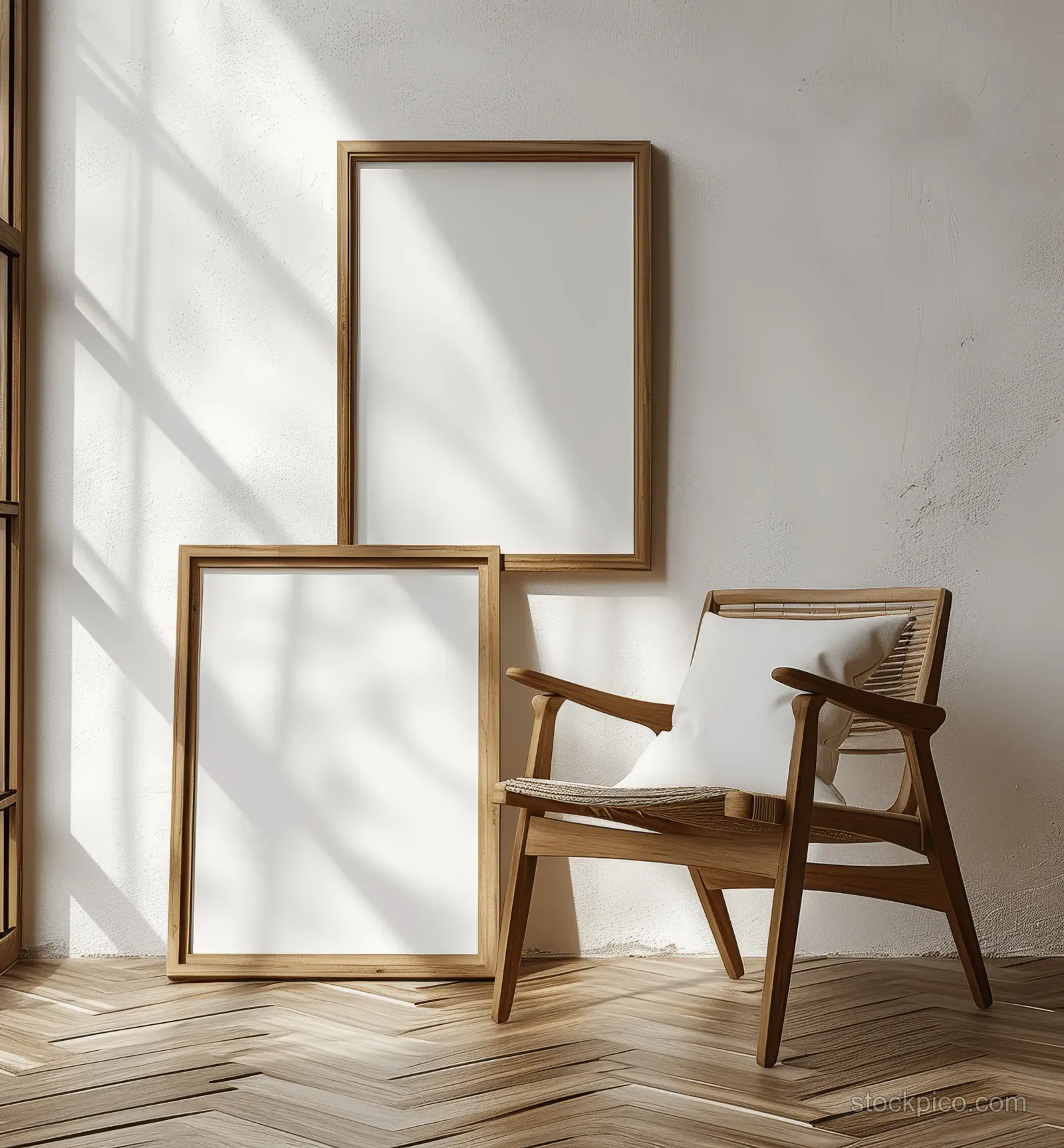 Two blank wooden frames lean against a white wall beside an empty chair on light oak parquet flooring.