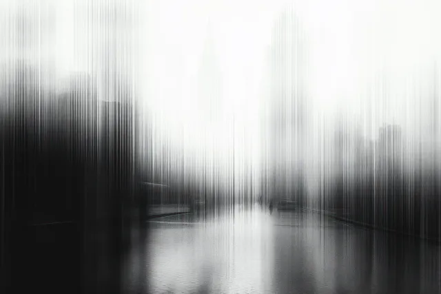 Monochrome skyline reflected on calm water with tall buildings blurred into vertical streaks.