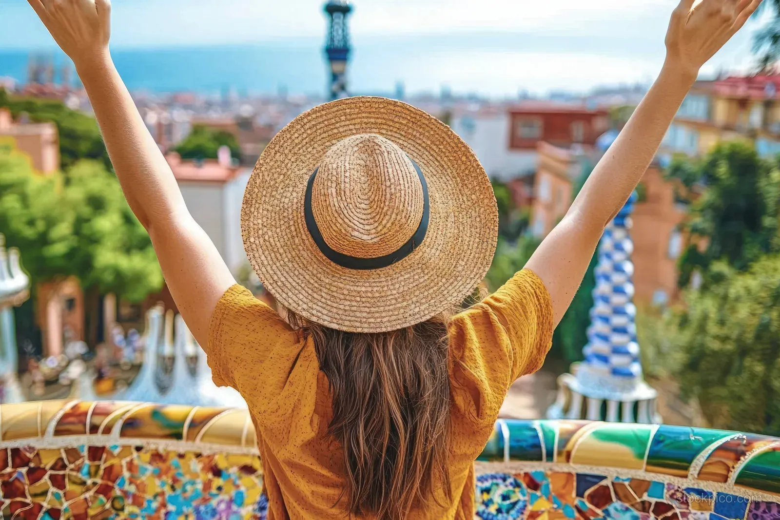 A smiling traveler raises arms for a selfie on a colorful mosaic terrace at Park Güell with Barcelona city views.