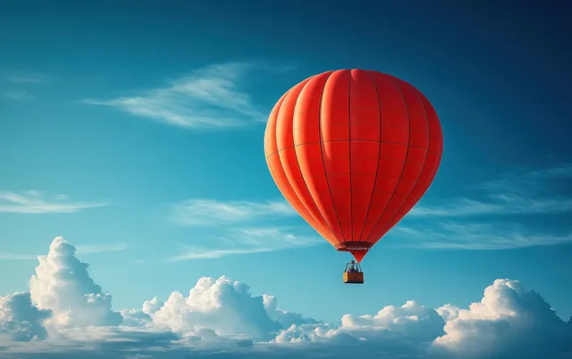 A red hot air balloon floats above white clouds under a deep blue sky.