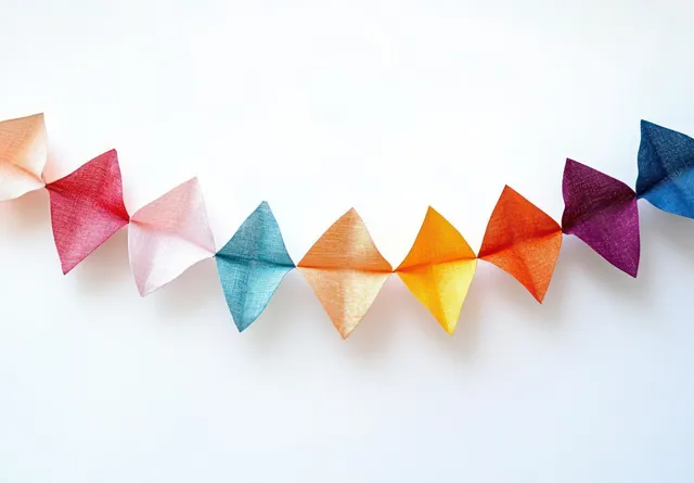 Triangular translucent fabric pennants form a colorful garland strung across a white background.
