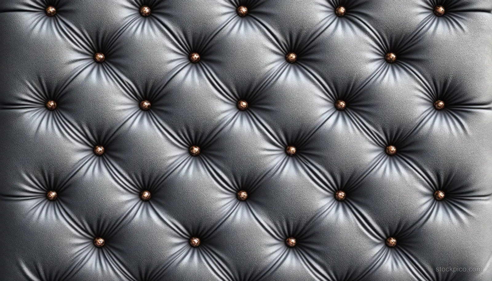Close-up of a tufted leather wall panel with diamond stitching and small button studs under soft lighting.