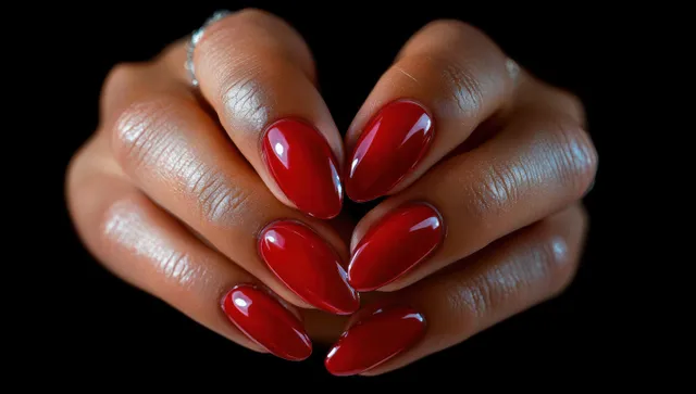 Hands with glossy red almond-shaped manicure nails and delicate rings holding fingers together on a black background.