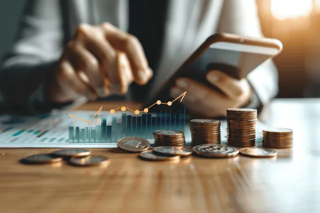 Business professionals using phones while analyzing ROI charts over coins and documents