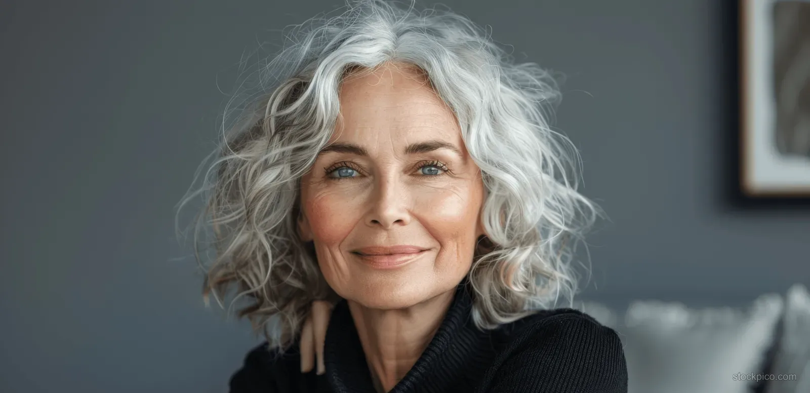Smiling senior Black woman with curly grey hair looks away against a gray studio background.