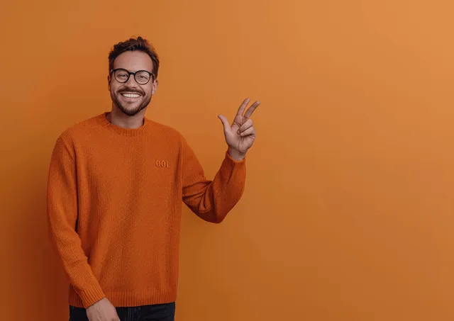 Happy man in glasses and orange sweater making OK gesture on warm beige background