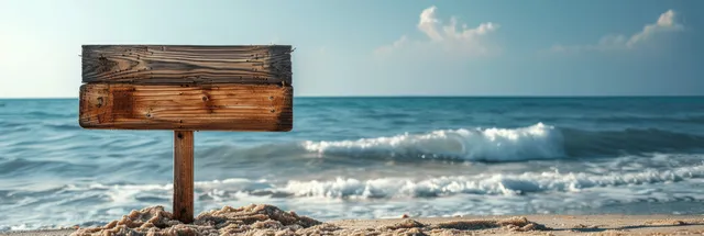 A weathered wooden signpost on a sandy beach with ocean waves and a blue horizon in the background.