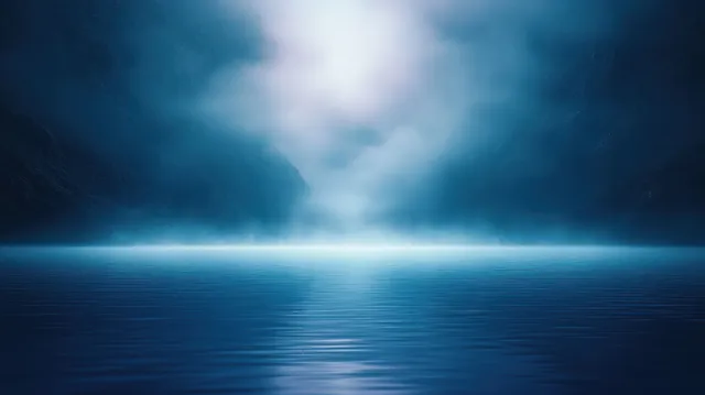 Misty blue seascape with a glowing horizon light beam reflected across calm water.