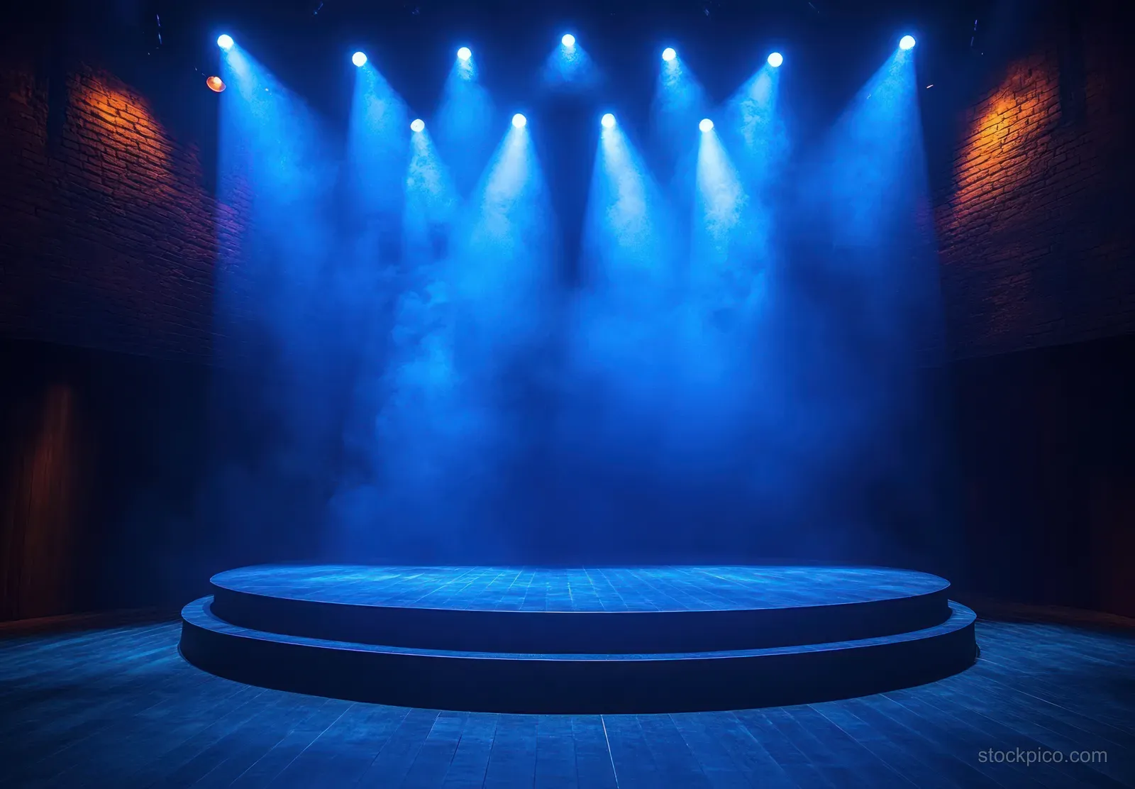 An empty circular stage in a dark theater is illuminated by blue spotlights with visible fog drifting above it.
