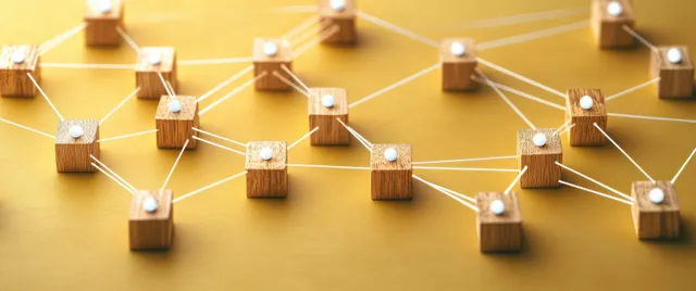 Wooden people figurines are connected with glowing network lines over a warm desk-like background.