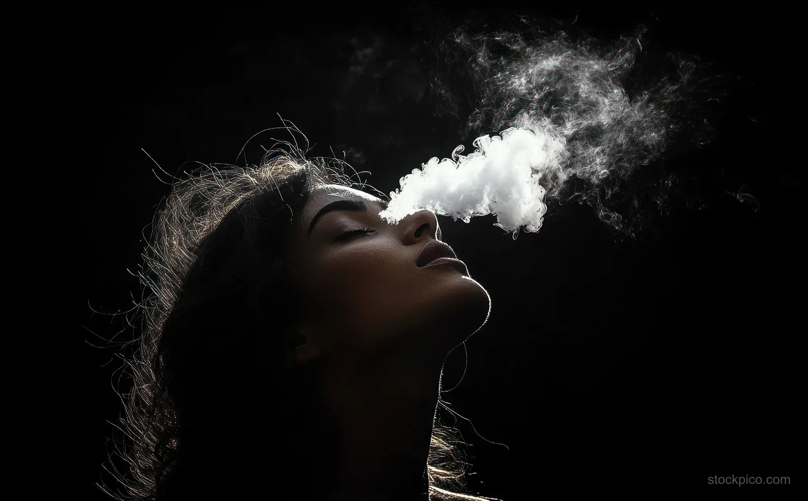 Silhouette of a woman exhaling a thick cloud of smoke with closed eyes against a dark background.