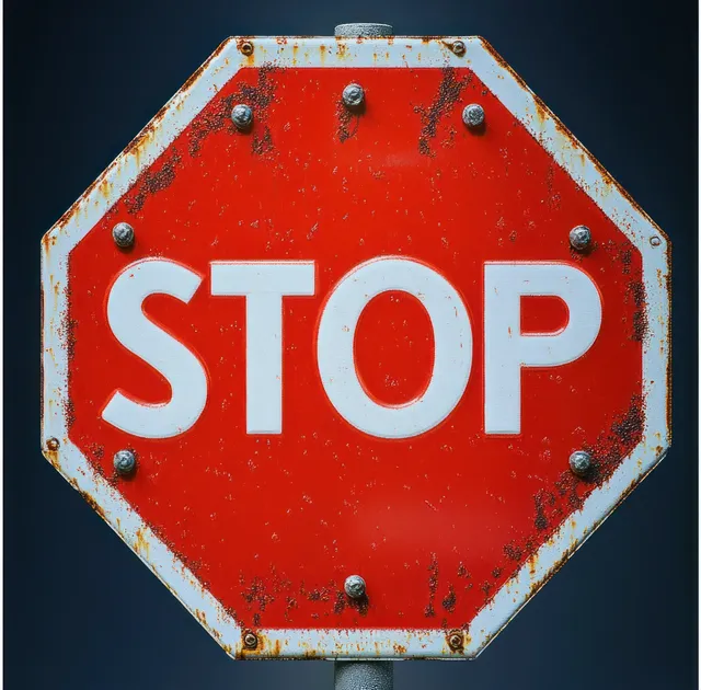 Close-up of a weathered red octagonal STOP sign with rusted bolts against a dark background