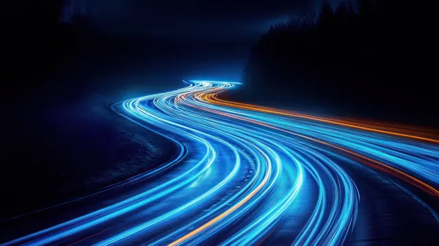 Curving night road with blue and orange light trails streaking through dark forest