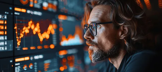Businessman reviewing financial charts on a tablet beside glowing candlestick charts on a large monitor.