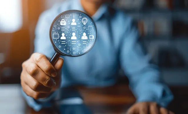 Hand holding magnifying glass over human icon dashboard for HR recruitment analytics
