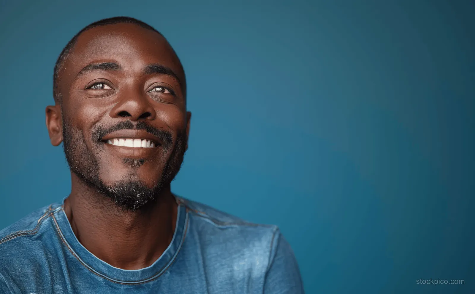 Smiling bald African American man laughing in a bright blue shirt, isolated on a cyan studio background.