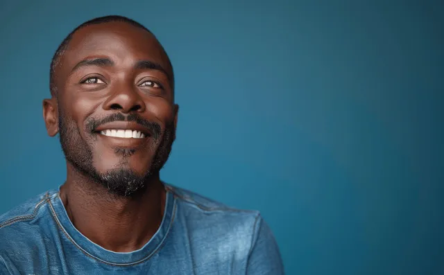 Smiling bald African American man laughing in a bright blue shirt, isolated on a cyan studio background.