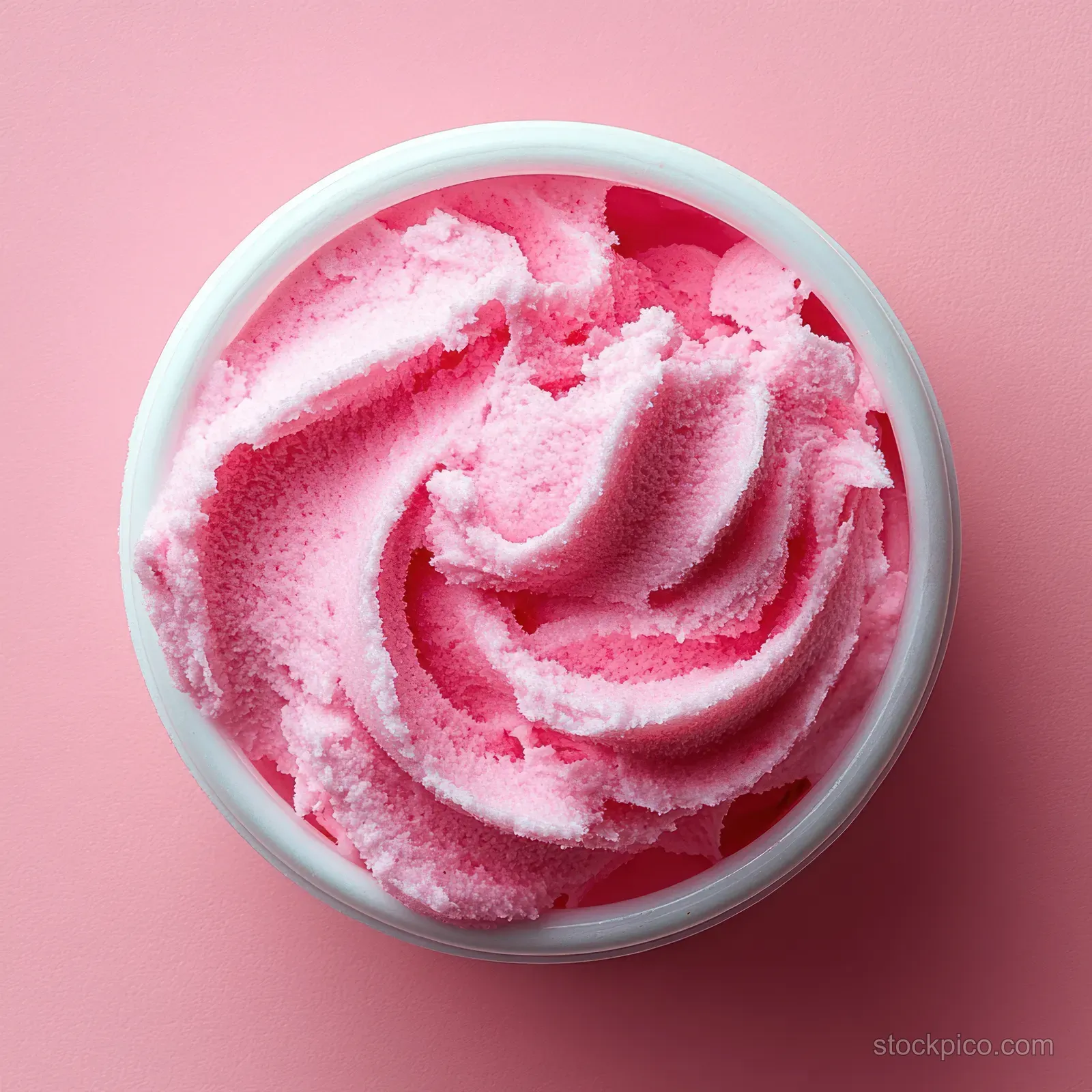Pink exfoliating scrub with a whipped texture in a white jar on a pastel pink background.