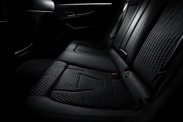 Black quilted leather rear seats with a seatbelt and nearby door handle inside a car cabin in dim light.