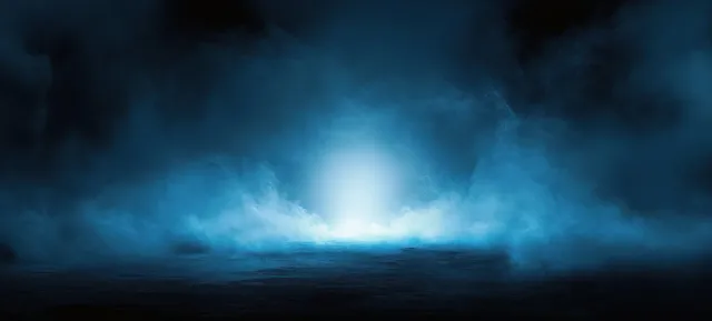 Blue fog rolls across dark ground around a glowing light source at night