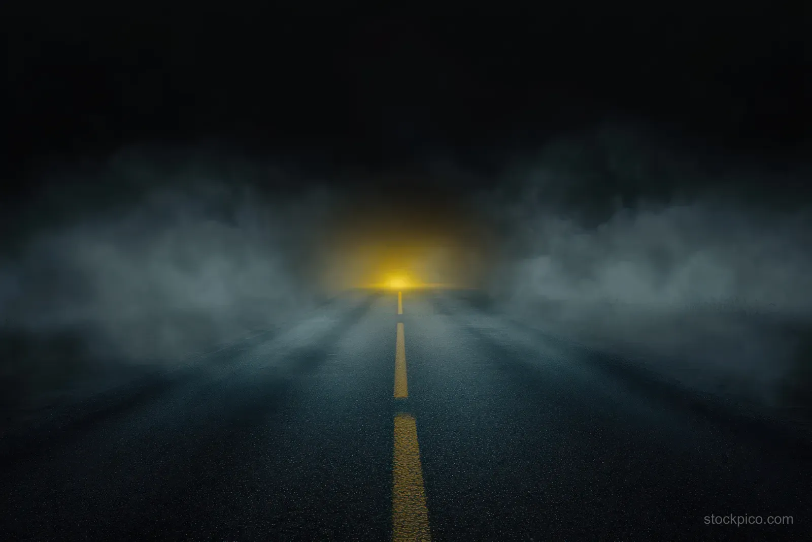 An empty dark road at night disappears into thick fog, with a fading yellow center line and distant hazy light.